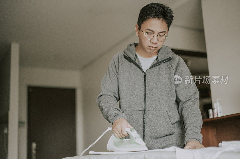 an asian chinese mid adult ironing his button down white shirt